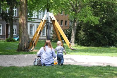 Mutter mit Kind sitzt auf Wiese vor Spielgerät im Grüngürtel von Kempen © Stadt Kempen / Christoph Dellmans