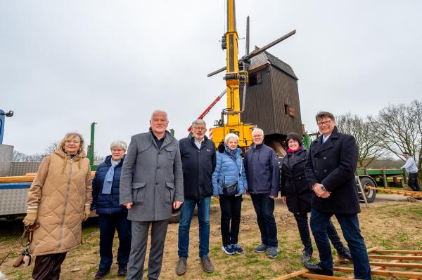 Montage Mühlenflügel Tönisberg 8 beteiligte Menschen stehen vor Bockwindmühle, an der ein Kran die Mühlenflügel anbringt