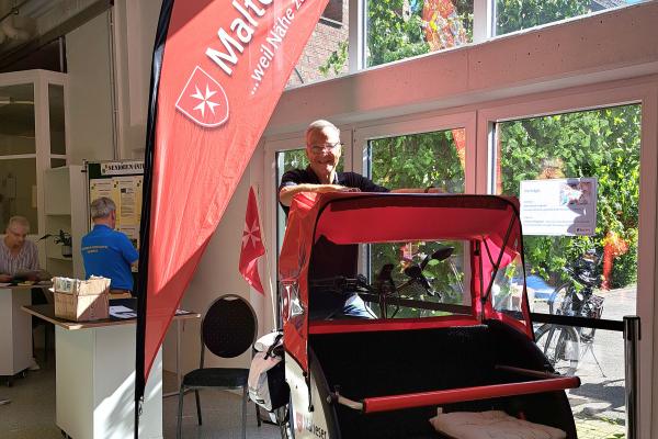 Ehrenamtlicher des Malteser Hilfsdienstes sitzt auf einer Fahrrad-Rikscha