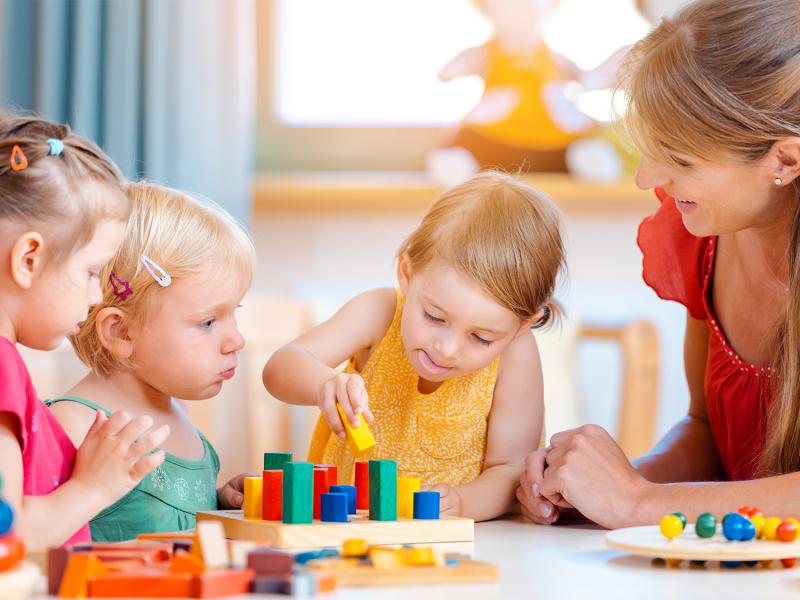 Kinder und Erzieherin spielen am Tisch in einer Kita