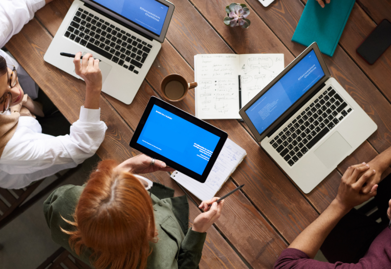 Menschen sitzen an einem Tisch und arbeiten mit Notebooks
